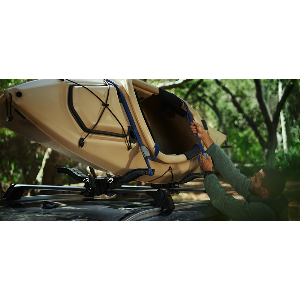 Person securing a beige kayak on a car roof with a forest in the background