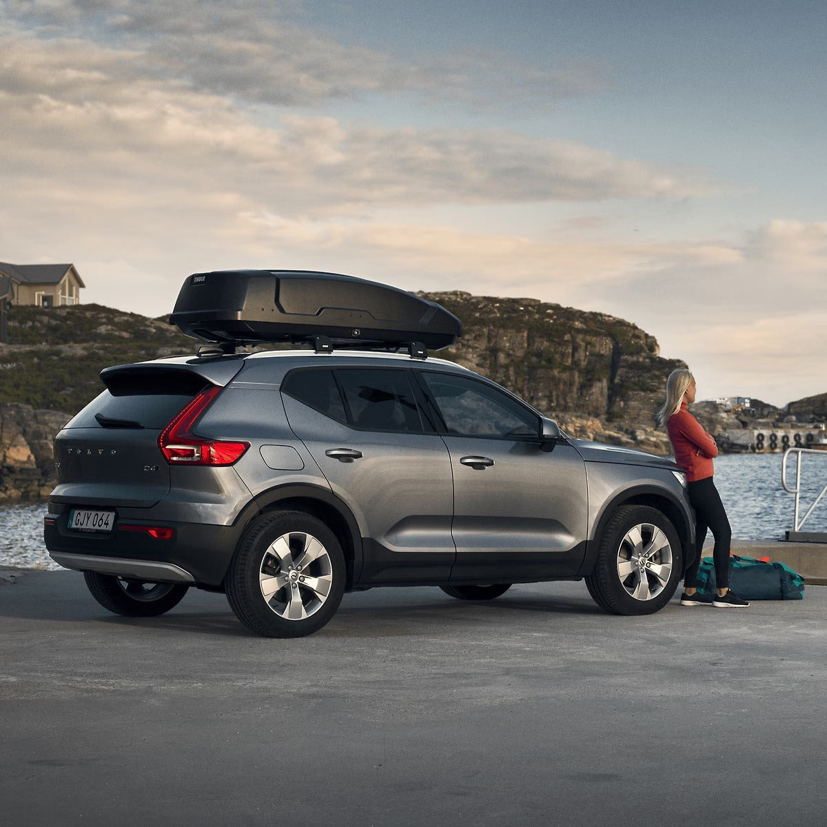 Car with a roof box parked by a waterfront with a person standing nearby.