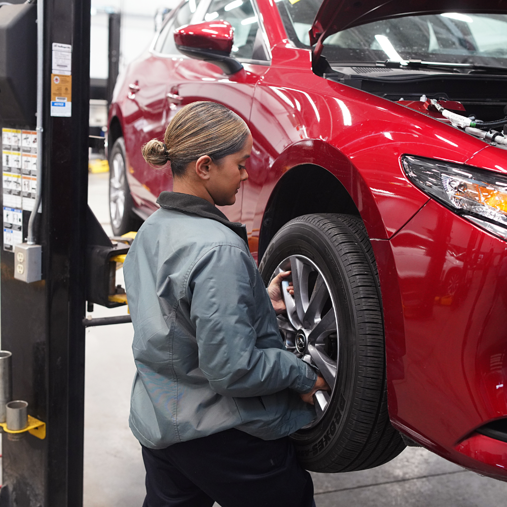 Person changing a tire on a red car in a garage.